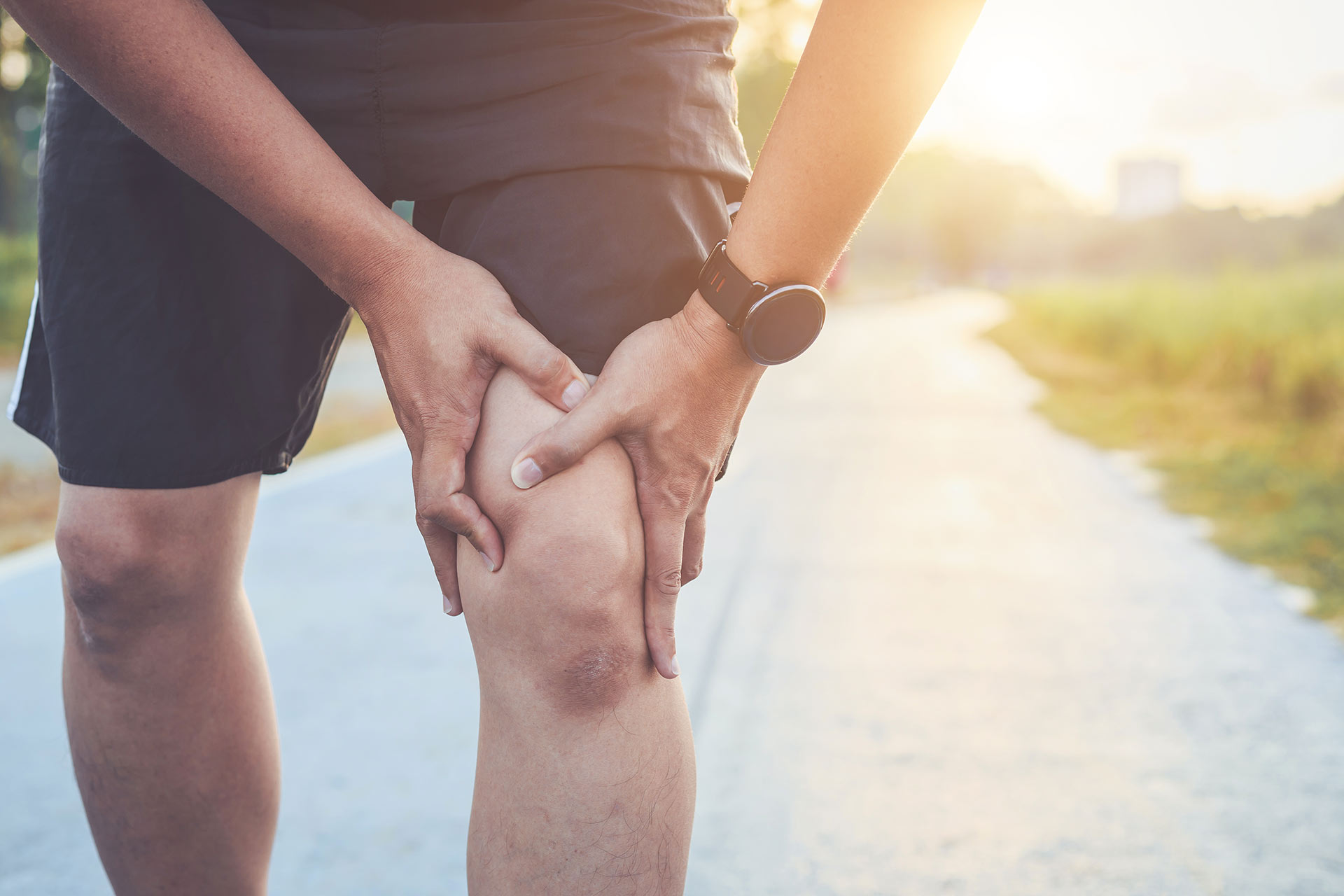 Man holding knee in pain while jogging outdoors