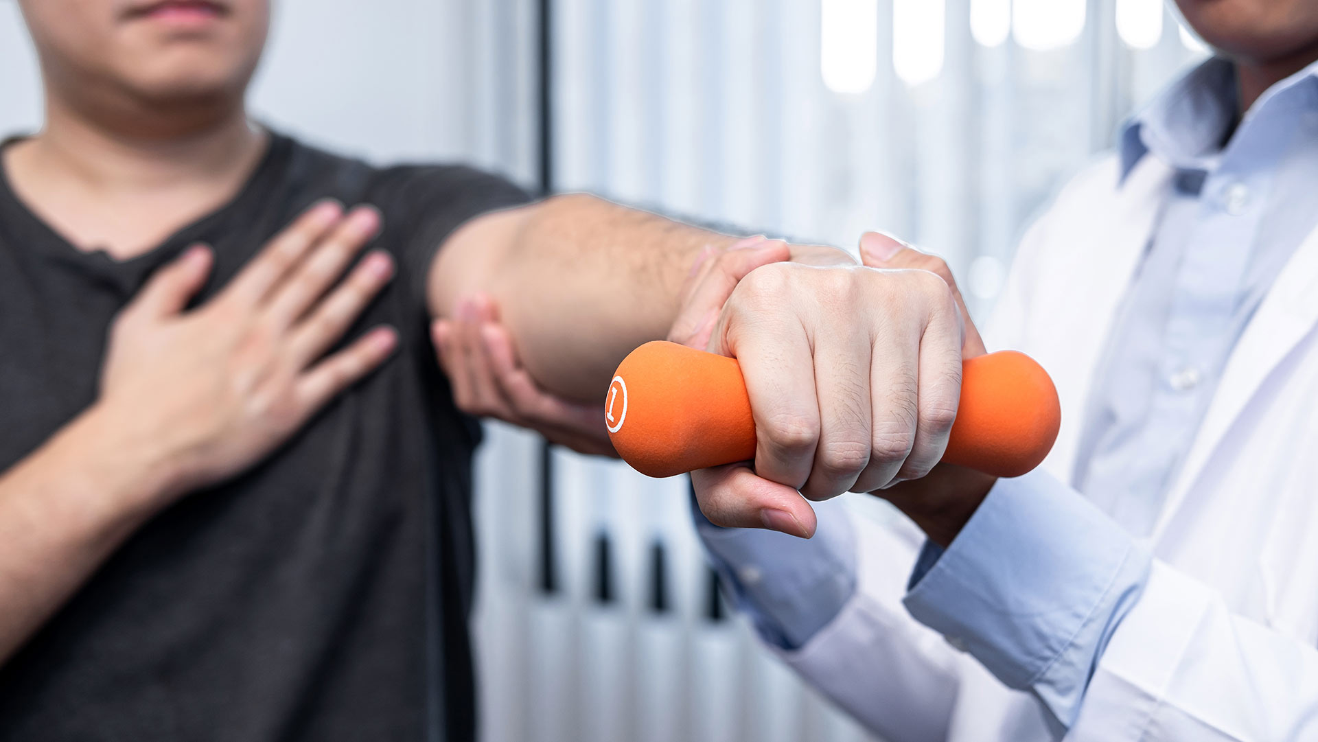 Physical therapist working on a man's shoulder while the patient is holding a small weight