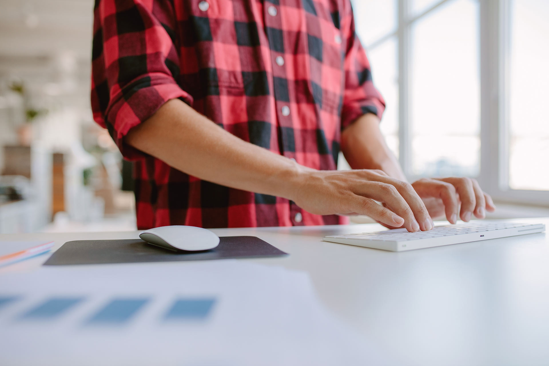 Person wearing red and black flannel shirt standing at a desk